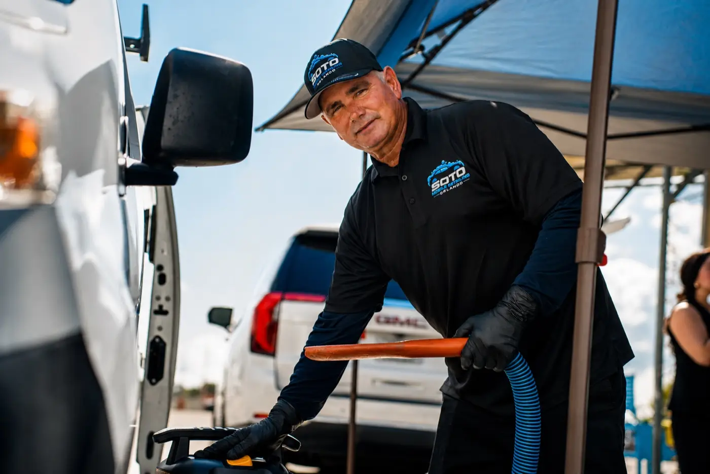 Mobile detailing company in Orlando, FL Soto detailer smiling while vacuuming a car under the mobile canopy