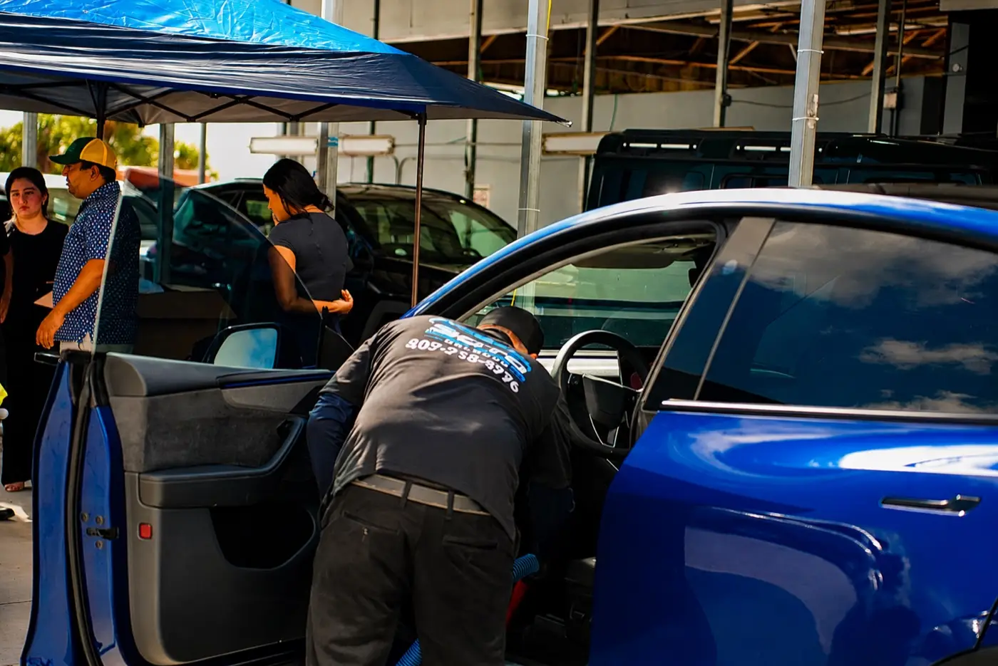 Mobile detailing company in Orlando, FL · founder section Mobile detailing company in Orlando, FL · detailer working the open door of a blue car under the mobile canopy